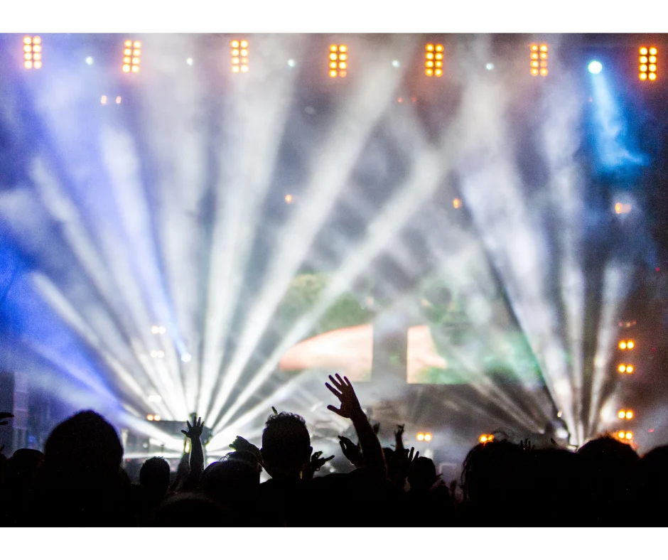 lights on a stage shine whilst the audience is in the dark, arms in the air